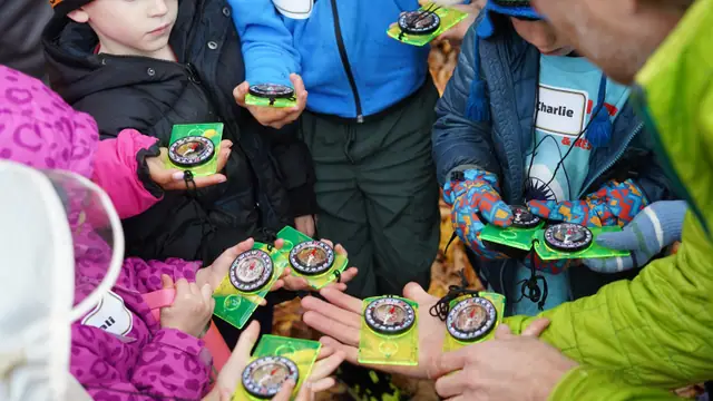 Hands hold compasses in a circle while an instructor points the way.