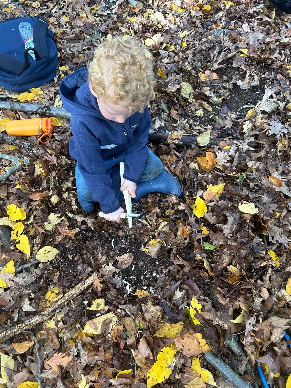 A kid kneels in fall leaves, working a ferro rod over a pile of tinder.