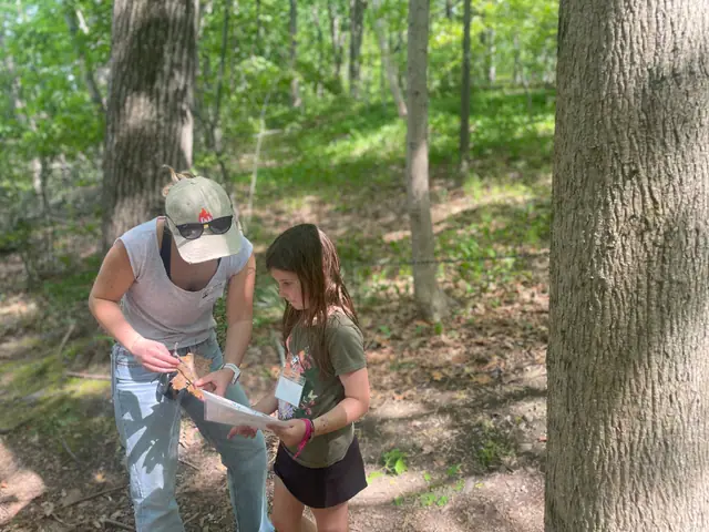 An instructor guides a kid's hands on a tool in the woods.