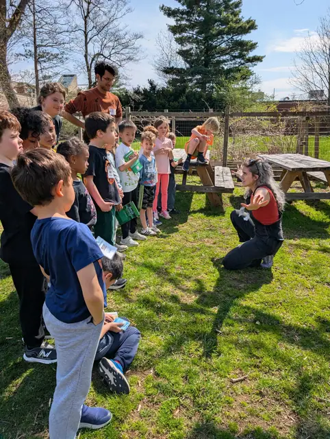 A line of kids on the grass with an instructor at the head, listening.