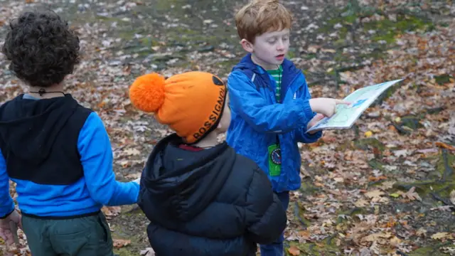 Three kids study a map together in the woods.