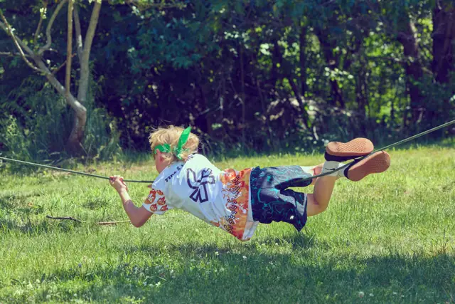 A kid crosses a rope strung between two trees at the Fire & Knives Games.