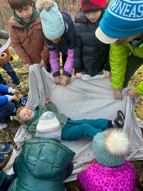 Kids carry a classmate on a tarp stretcher during first-aid practice.